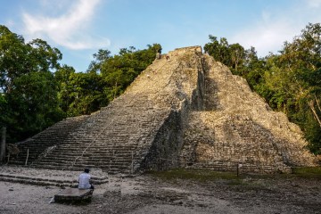 a group of people sitting on a rock with Coba in the background
